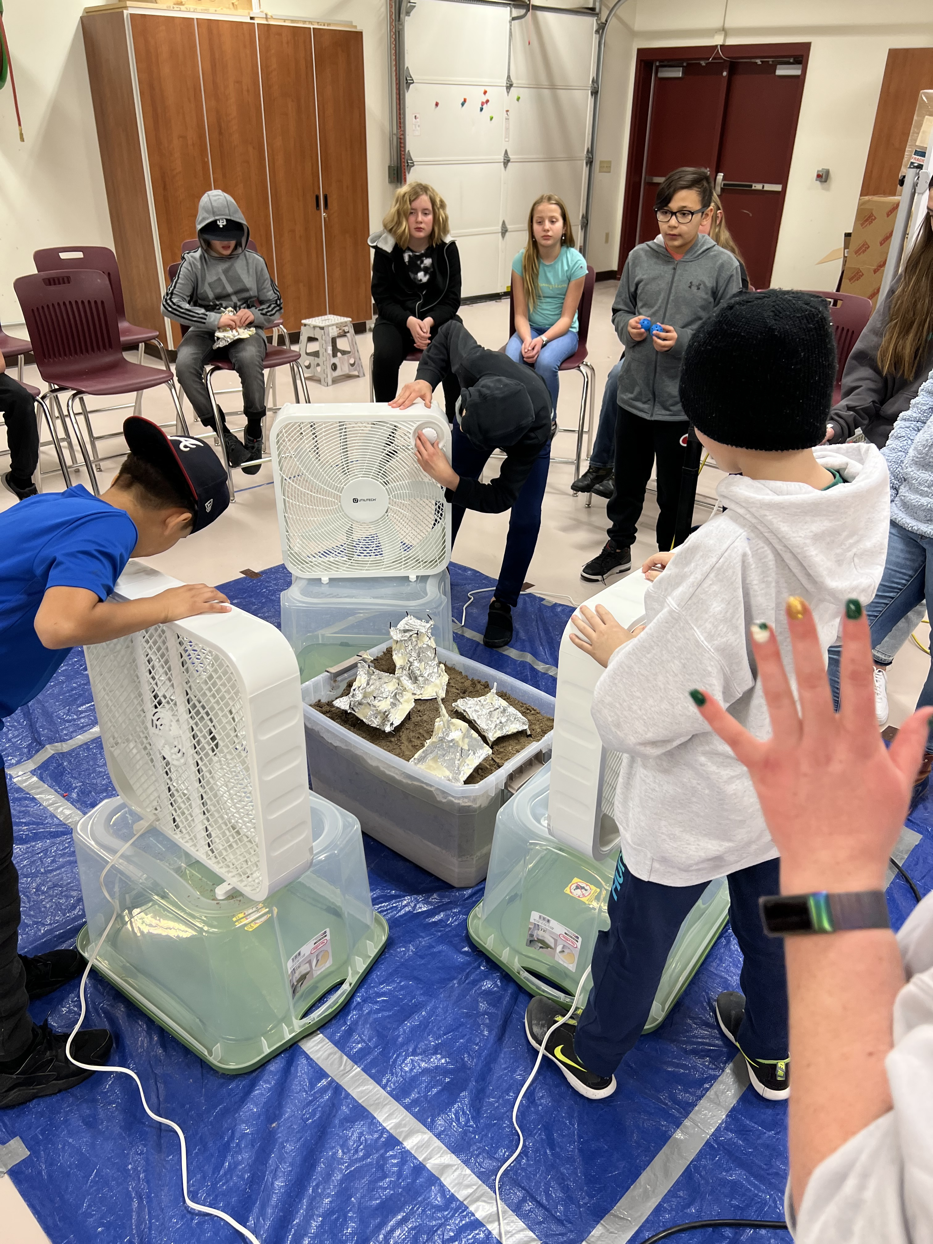Students using fans to simulate hurricanes on cardboard houses