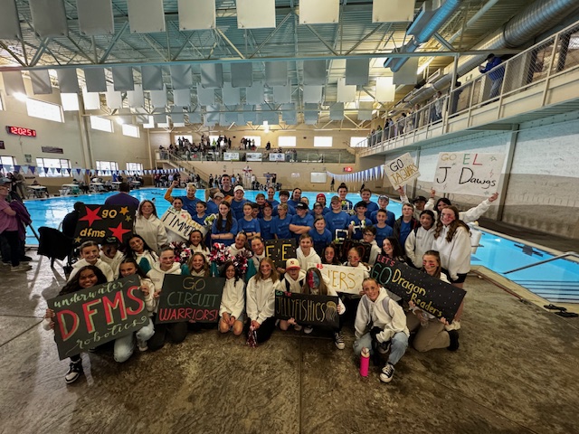 Student holding their robots by large pool surrounded by student council members holding signs. 